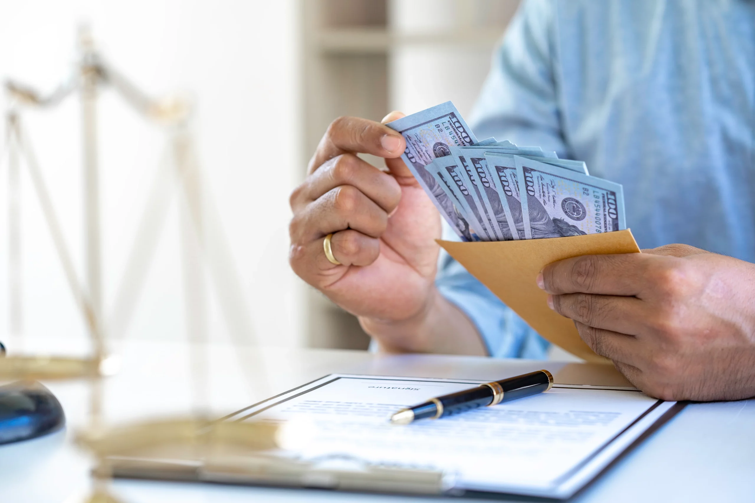 Person holding an envelope filled with hundred-dollar bills beside a legal contract, pen, and scales of justice, representing a Missouri debt collection class action lawsuit and consumer financial rights.