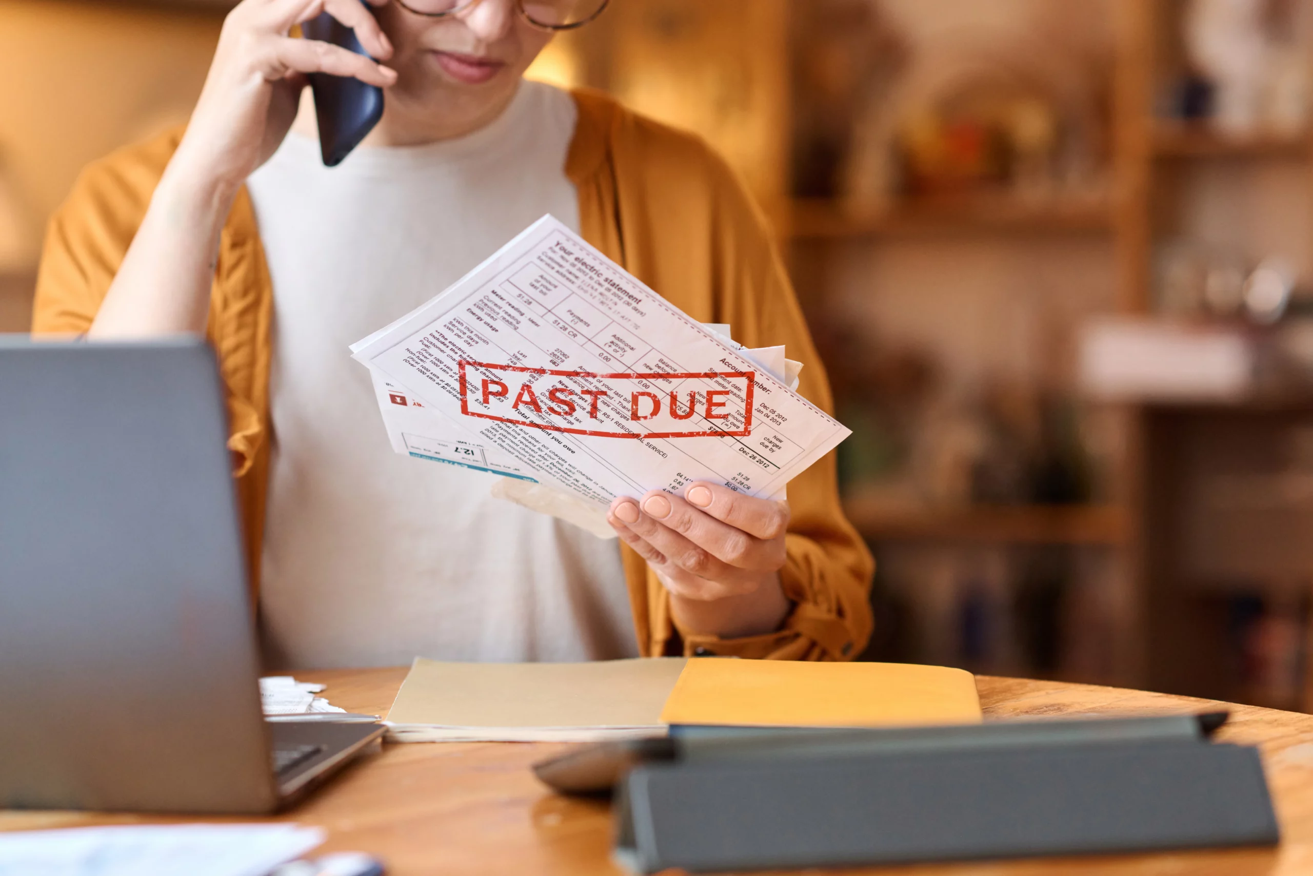 Concerned consumer holding past-due bills while speaking on the phone, representing Missouri FDCPA debt collector rights and protection against abusive debt collection practices.